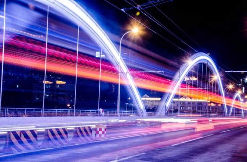 Een foto met lange sluitertijd van een weg bij nacht met verlichte bogen met neonachtige lijnen