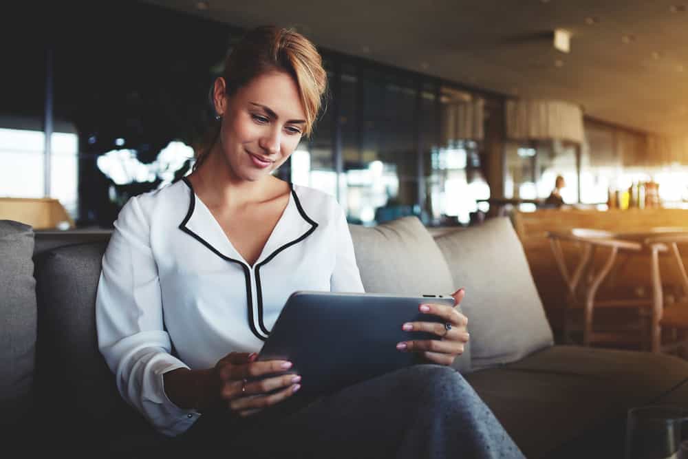 Een blonde vrouw met een wit shirt zit op een bank en kijkt op haar tablet|Sanoma zet co-creatie in voor nieuwe iPad apps